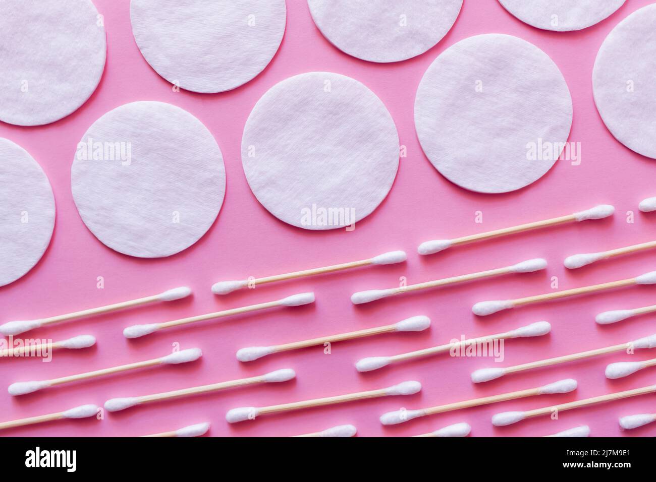 rows of white cotton pads and ear sticks on pink background, top view Stock Photo