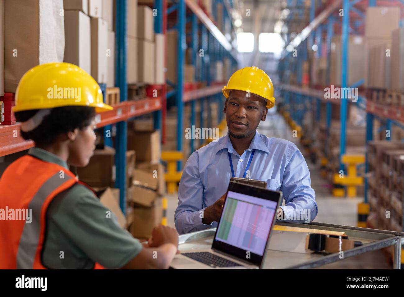 African american young man looking at young female coworker using laptop on table in warehouse Stock Photo