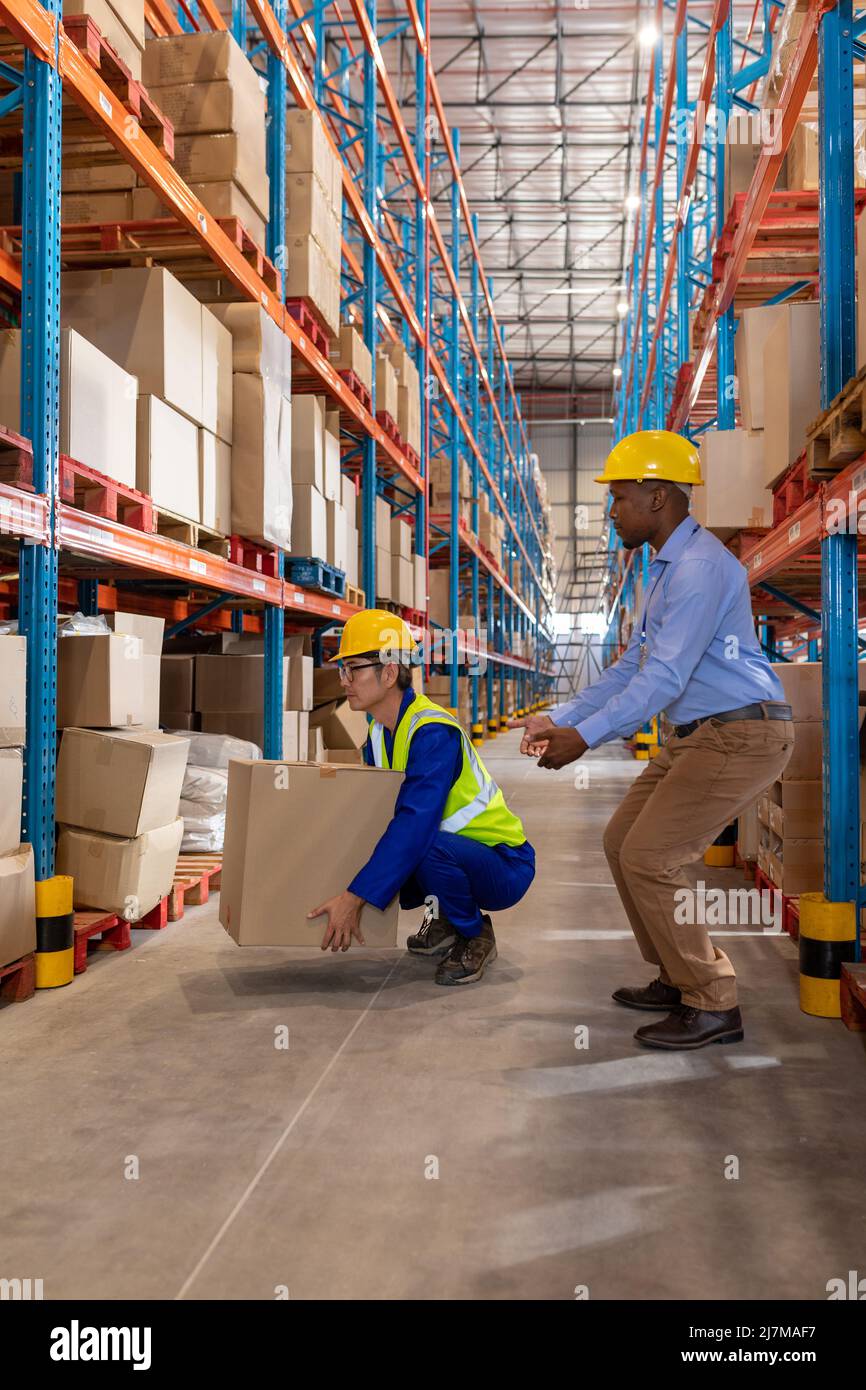 African american young foreman gesturing while guiding asian mature man lifting cardboard box Stock Photo