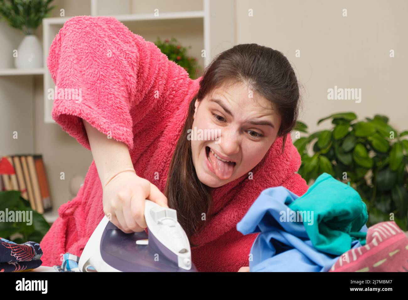 A crazy housewife in a pink robe diligently irons clothes with an iron