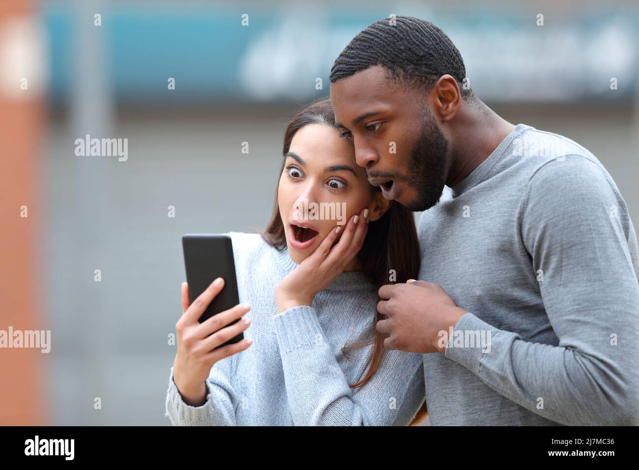 Amazed interracial couple checking cell phone news in the street Stock Photo