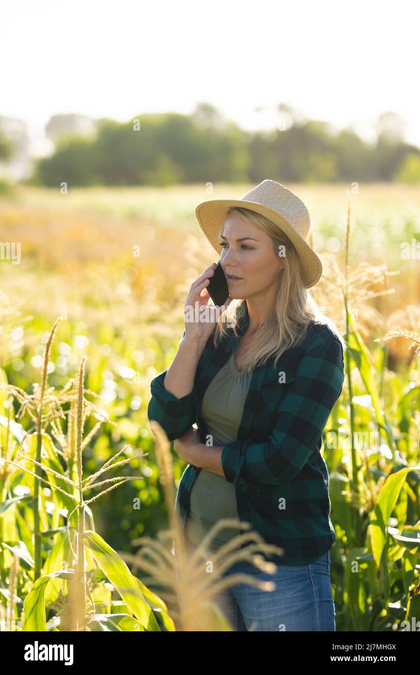 Serious caucasian mid adult female agronomist wearing hat talking over smartphone in organic farm Stock Photo