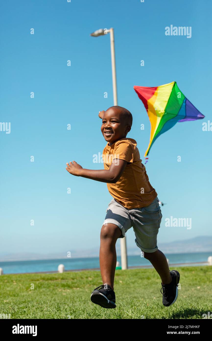 Happy african american boy running with colorful kite against clear