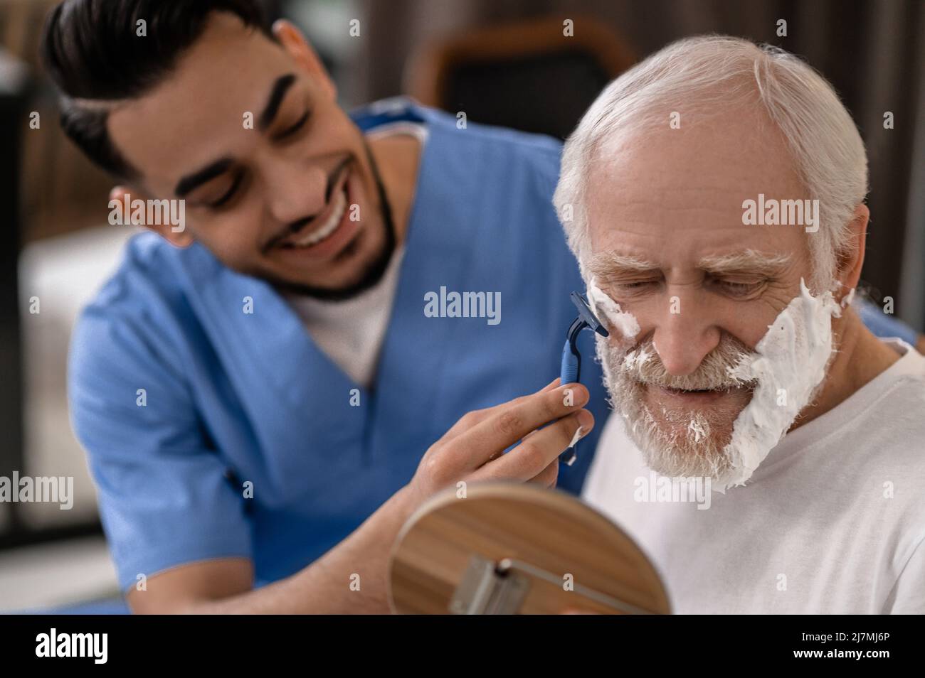 Cheerful volunteer giving an elderly person a shave Stock Photo