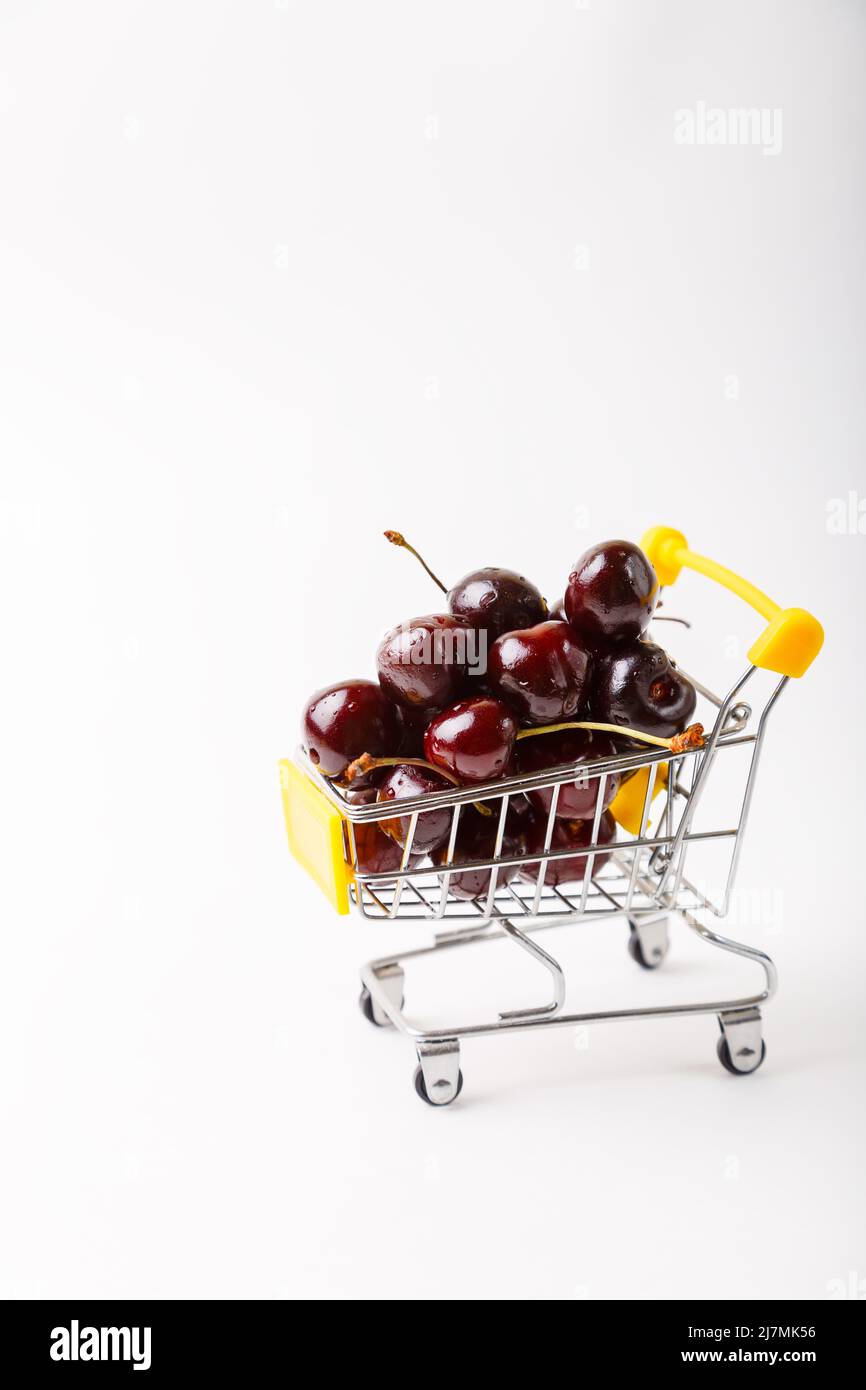 Cherry in a miniature (small) grocery cart for a supermarket. Toy cart with berries on a white background. Close-up, Copy space, banner. Stock Photo