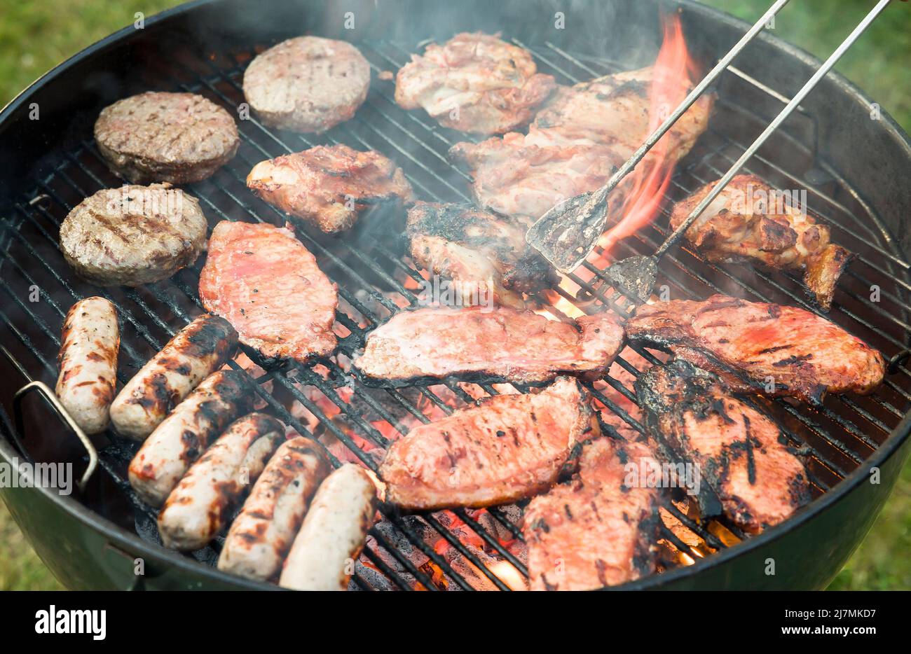 Barbecue cooking. Detail of meat cooking on a charcoal kettle home barbecue in a garden, UK Stock Photo