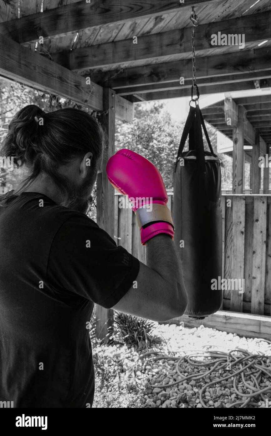 A man exercising in an outdoor home gym, using bright pink boxing gloves. Punching bag hanging from the above balcony. Stock Photo