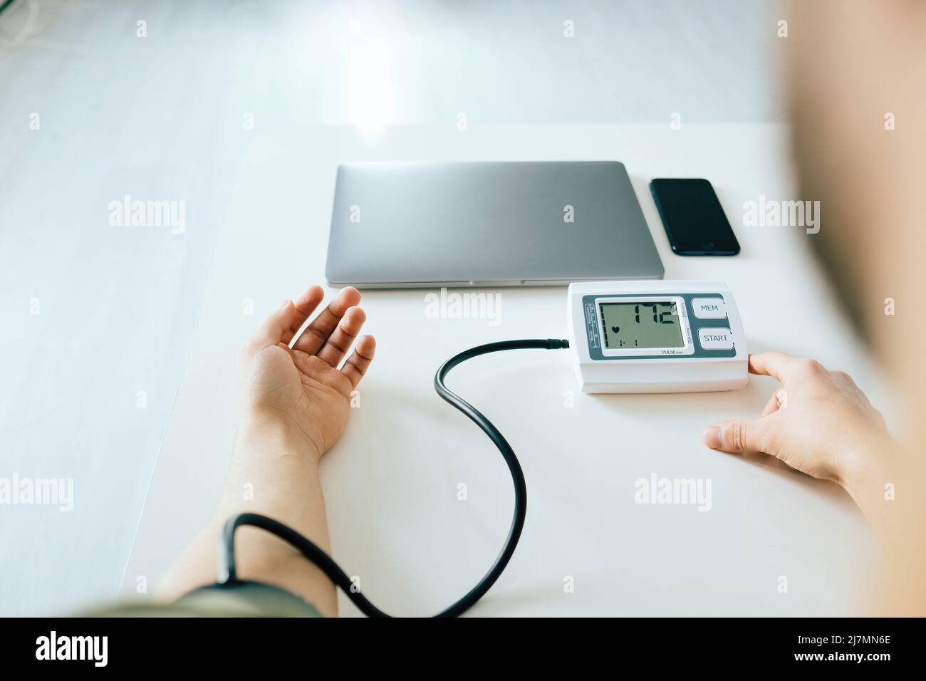 Over shoulder view of young man checking blood pressure at home. Using modern tonometer, experiencing hypertension caused by stress. Stock Photo