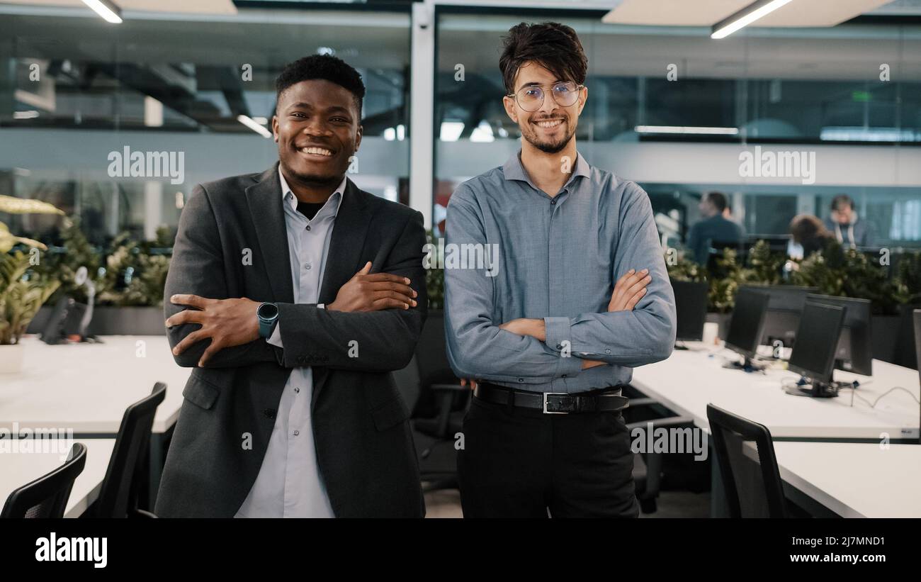 Multiracial couple of business colleagues smiling diverse co-workers arabian young man african manager businessman guy stand indoors posing together Stock Photo