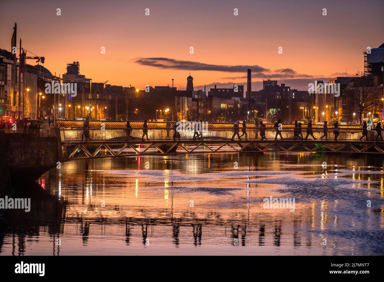 Commuters crossing a footbridge over a city river at sunset, Millennium bridge, , Quays, Temple bar, River Liffy, Dublin, ireland Stock Photo