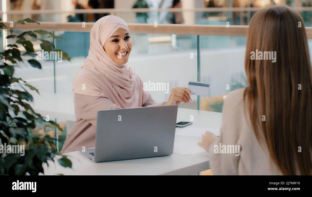 Muslim financial advisor banking worker giving credit card unrecognizable girl client signs contract for approval of bank loan takes mortgage arab Stock Photo