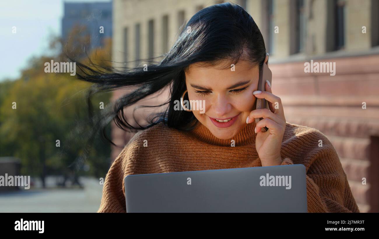 Young multitasking girl talking on telephone smiling answering friendly call orders Internet service in online store on laptop using computer Stock Photo