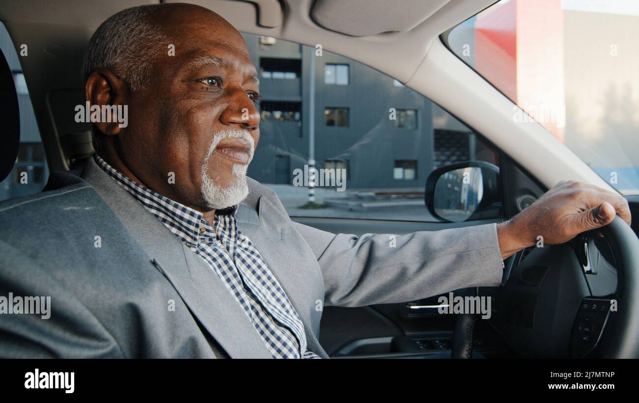 Elderly african american businessman driving automobile on roadway experienced confident driver carefully looks at road journey traveling mature man Stock Photo