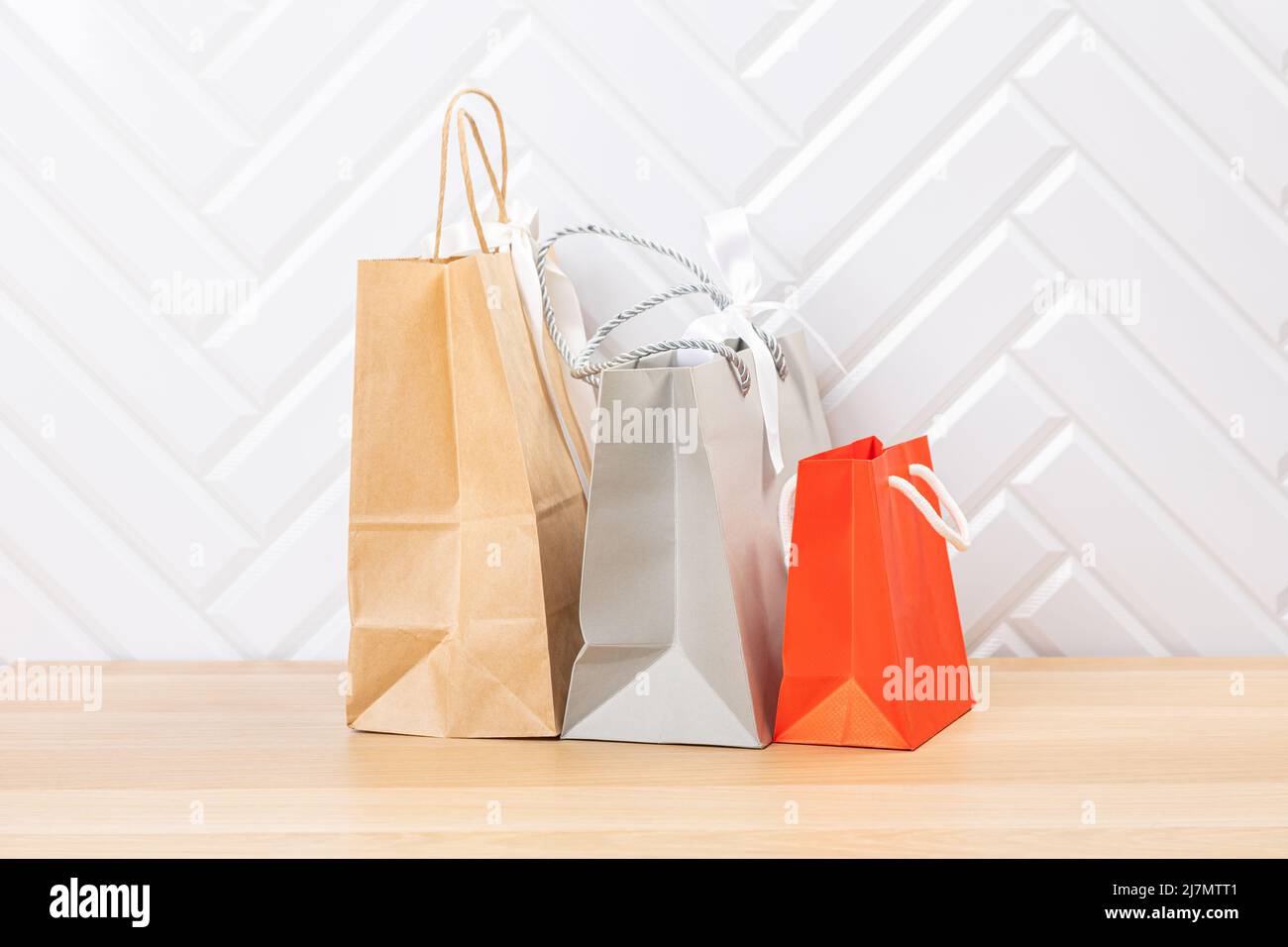 Blank  paper carrier bag with handles for shopping, facing front on right side of a wood veneer table with white wall background providing copy space Stock Photo