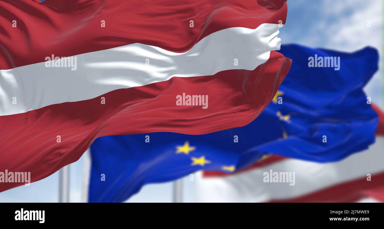 Detail of the national flag of Latvia waving in the wind with blurred european union flag in the background on a clear day. Democracy and politics. Eu Stock Photo