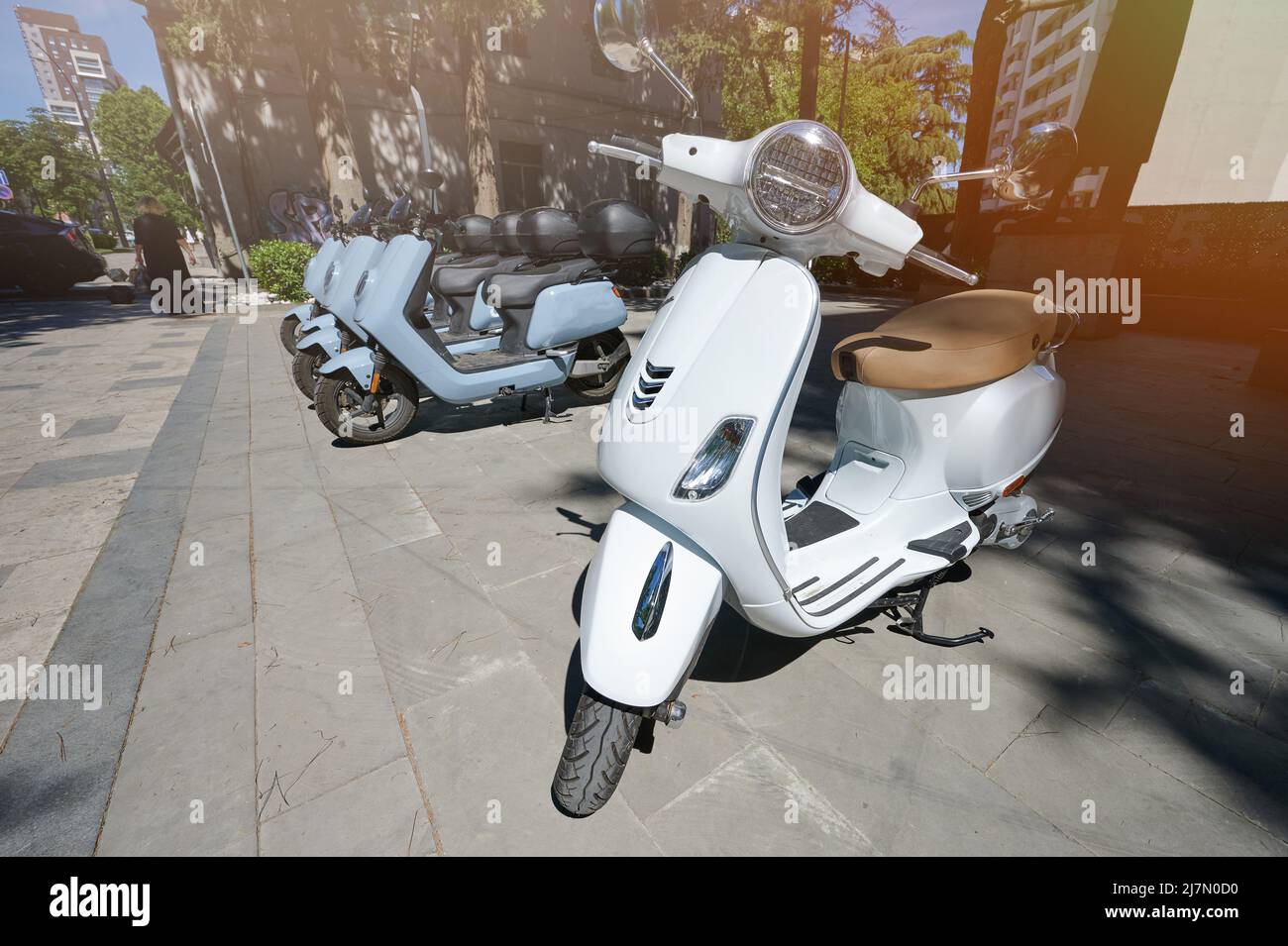 Moto scooters park in city street for rent on bright sunny day Stock Photo
