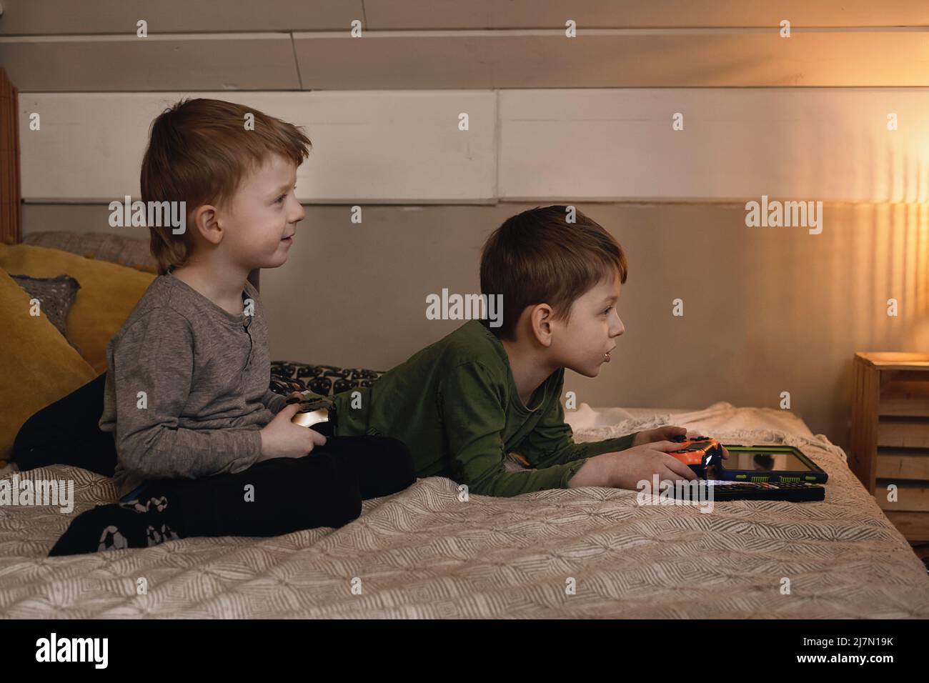 Kids playing video games at home on the bed at night. Boys using game console and having fun in the evening. Brothers using technologies exited. Boy Stock Photo