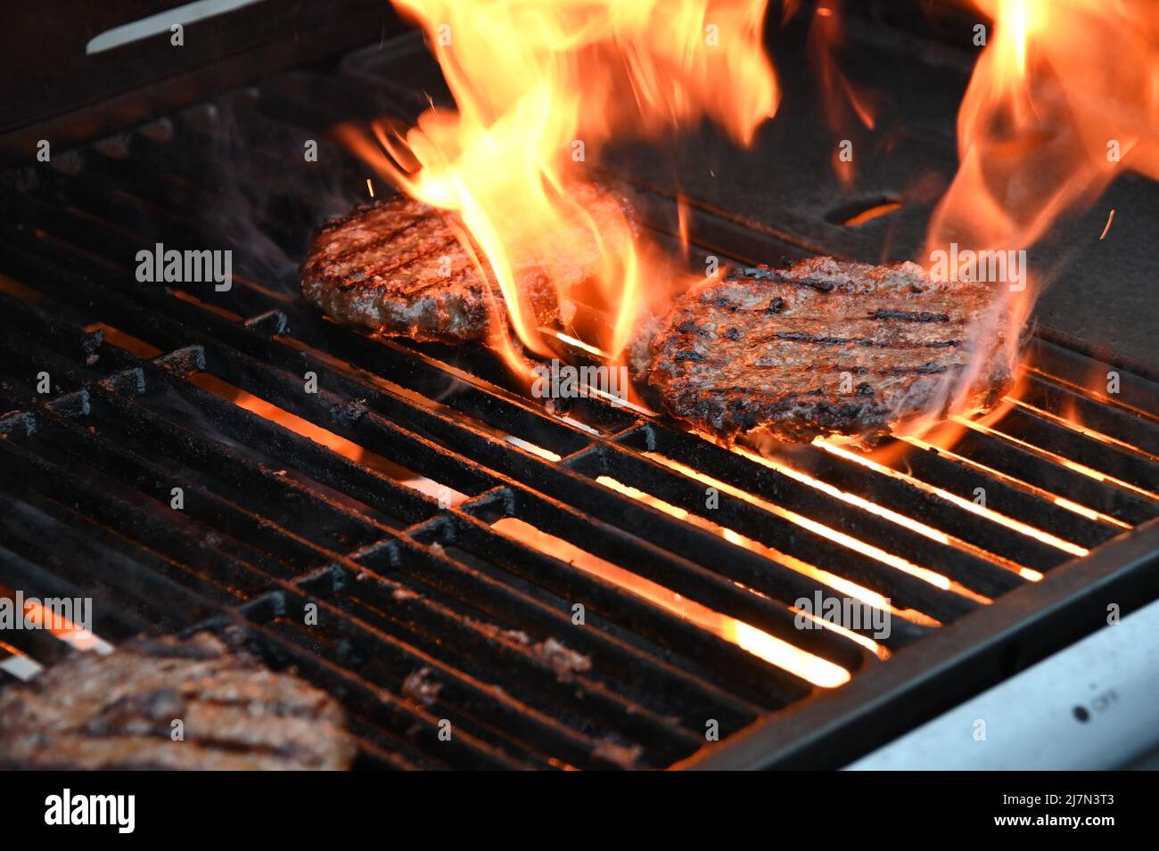 Flamed grilled beef burgers barbecued on an outdoor BBQ Stock Photo