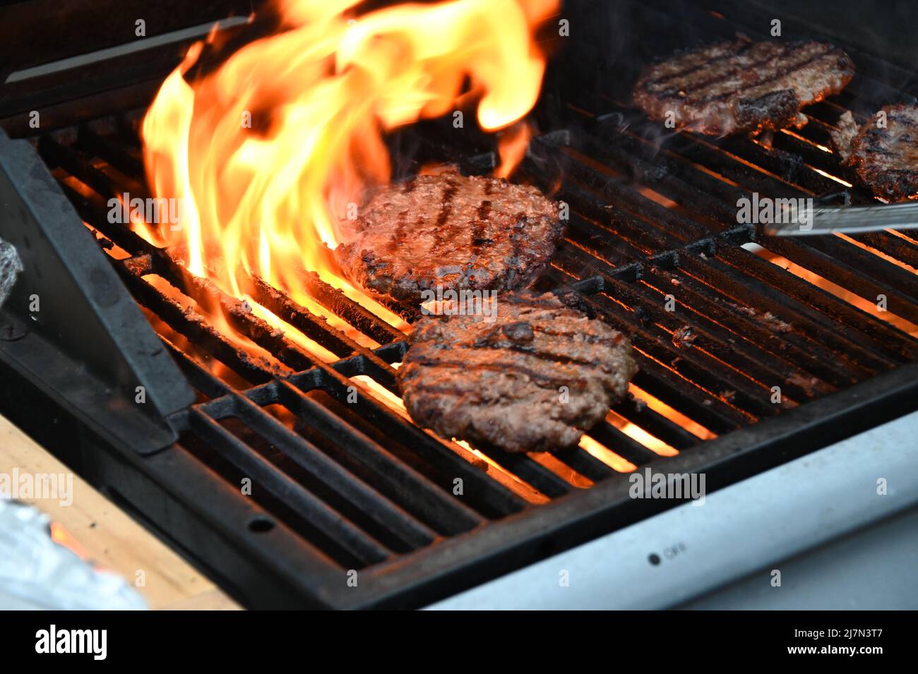 Flamed grilled beef burgers barbecued on an outdoor BBQ Stock Photo