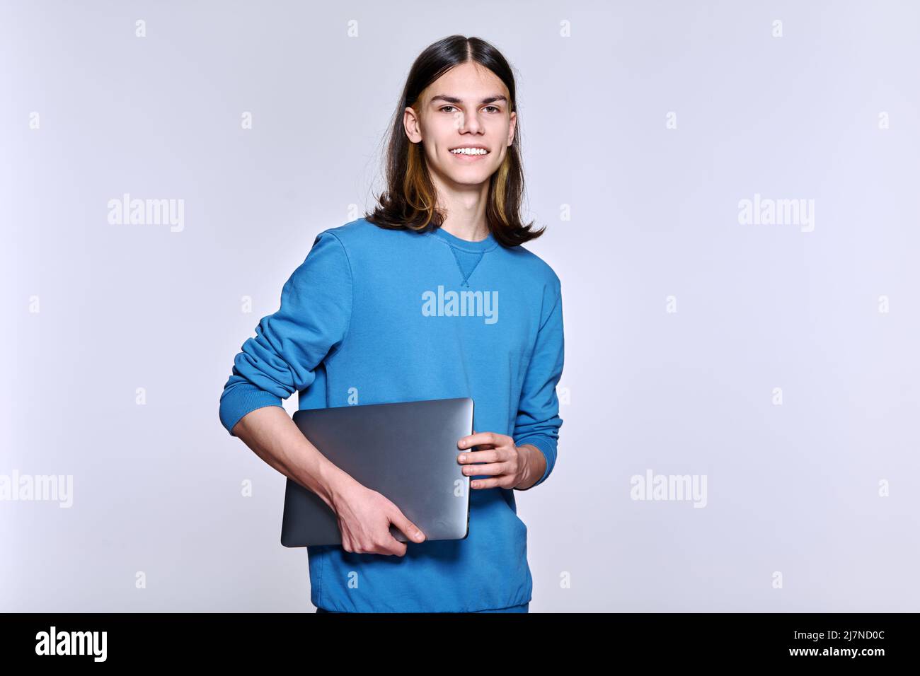 Portrait of positive teenage student guy with laptop looking at camera ...