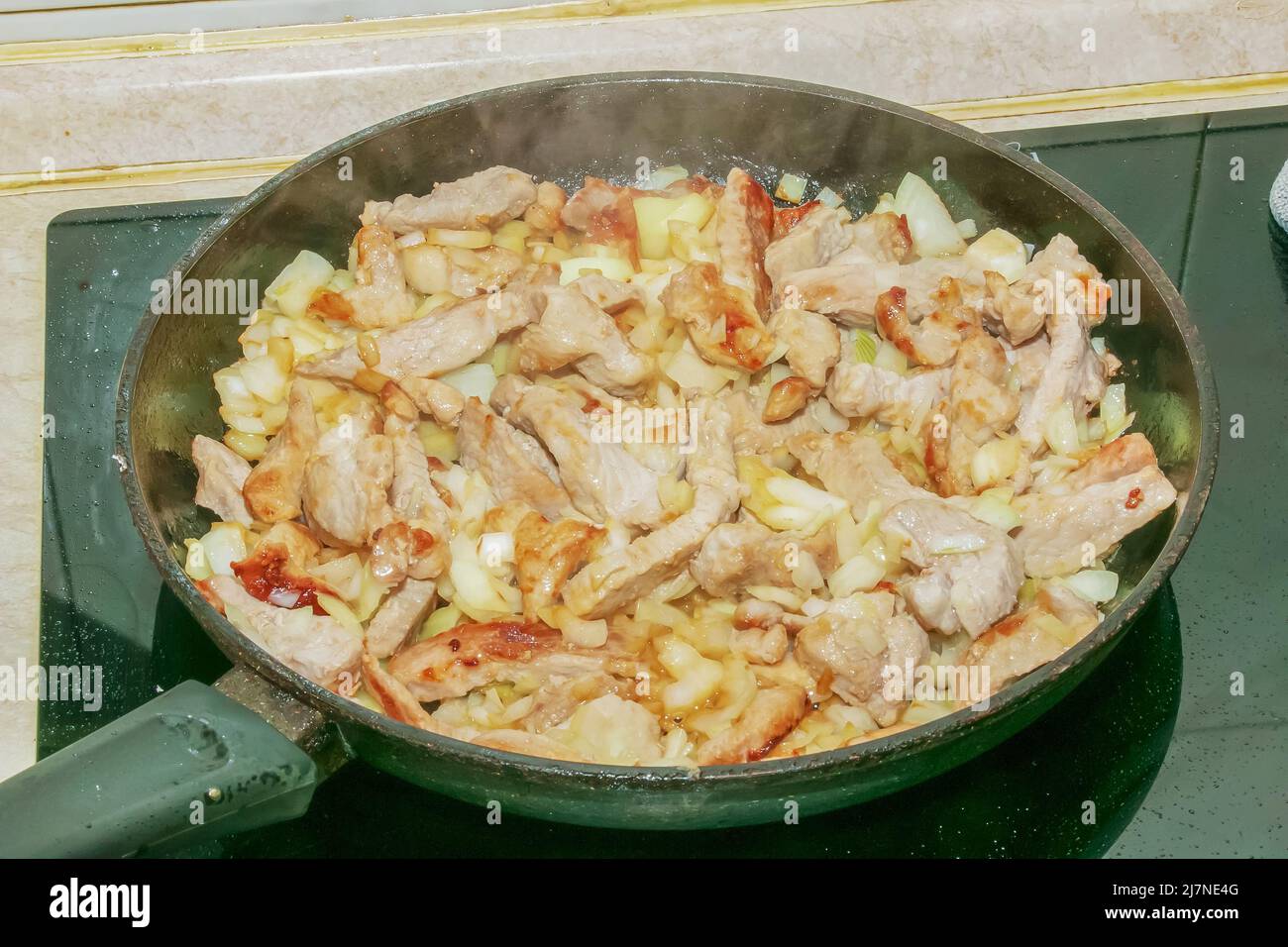 Pieces of pork and chopped white onion, fried in a hot pan with oil