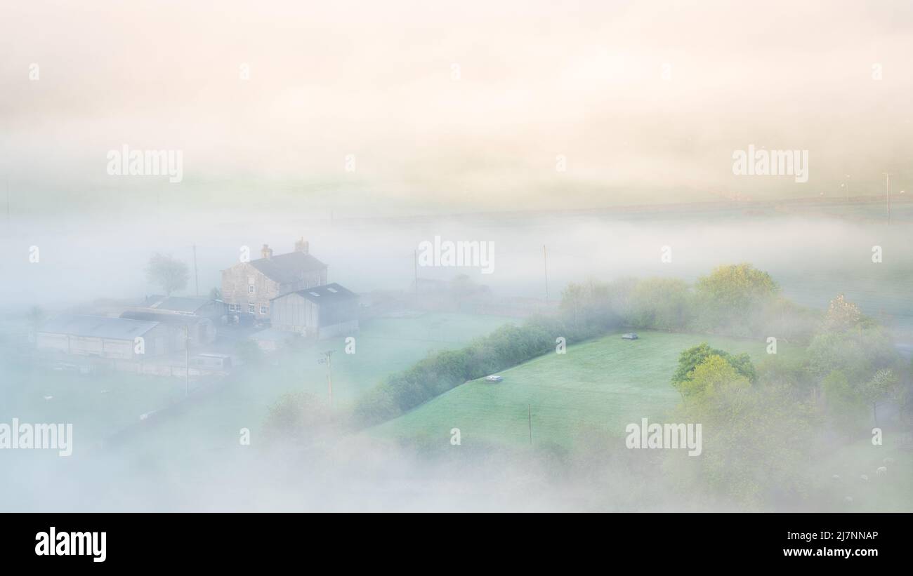 Hints of the patchwork landscape beneath Embsay Crag are visible as the fog ebbs and flows on a beautiful spring morning in North Yorkshire. Stock Photo