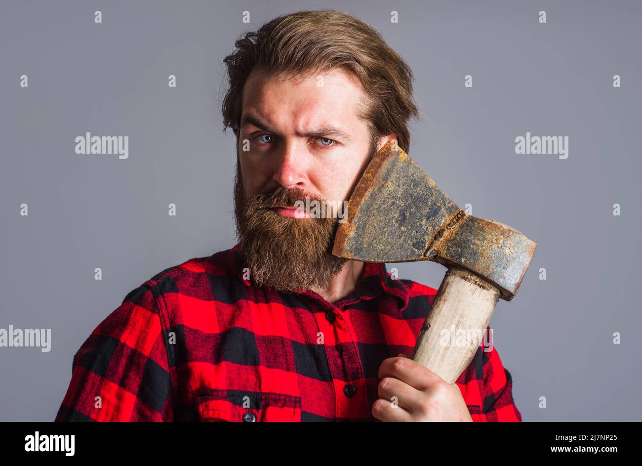 Bearded man with axe. Logger tool. Guy in checkered shirt with hatchet. Canadian lumberjack with ax. Stock Photo