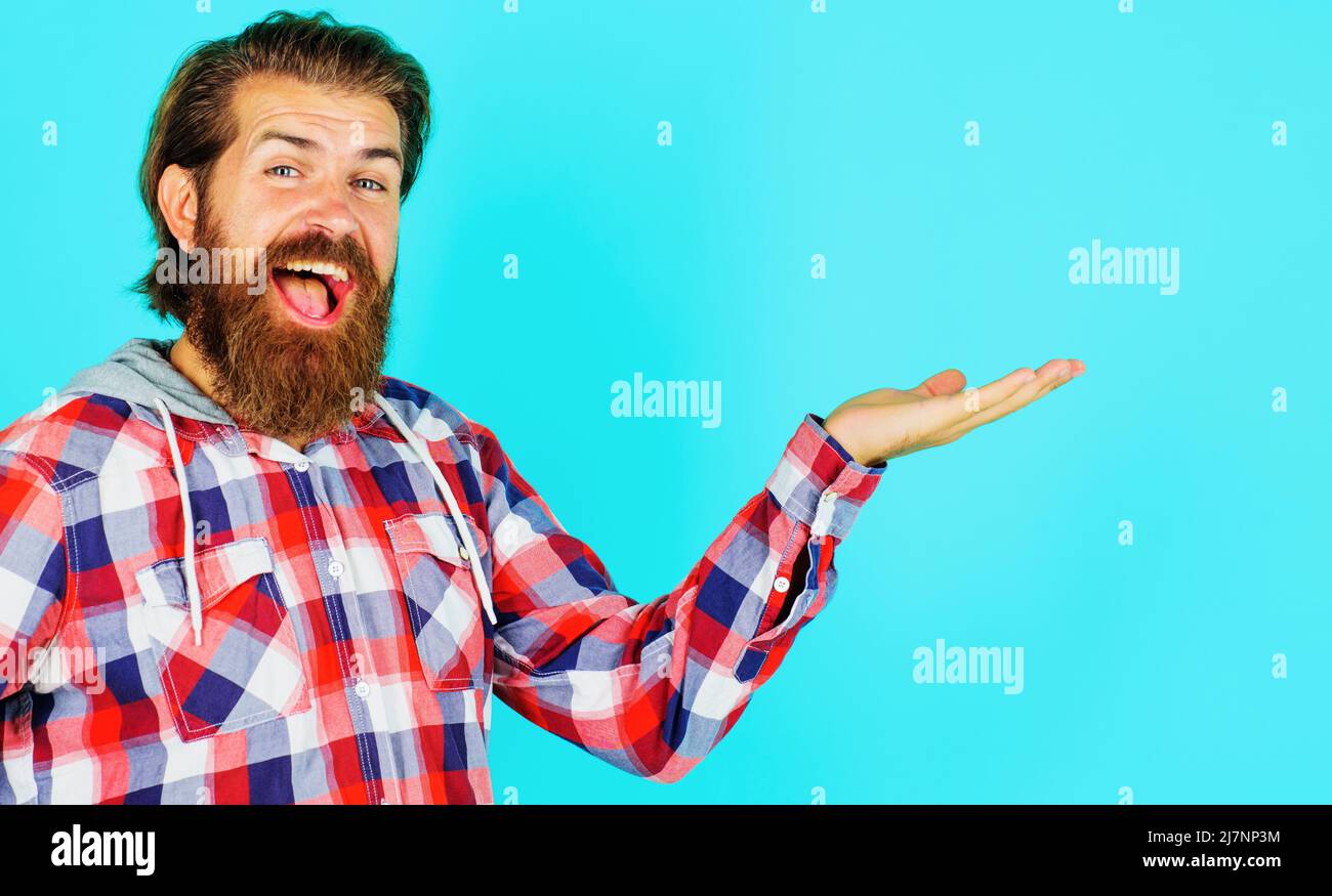 Happy bearded man in plaid shirt presenting product holds something on palm. Male show hand gesture. Stock Photo