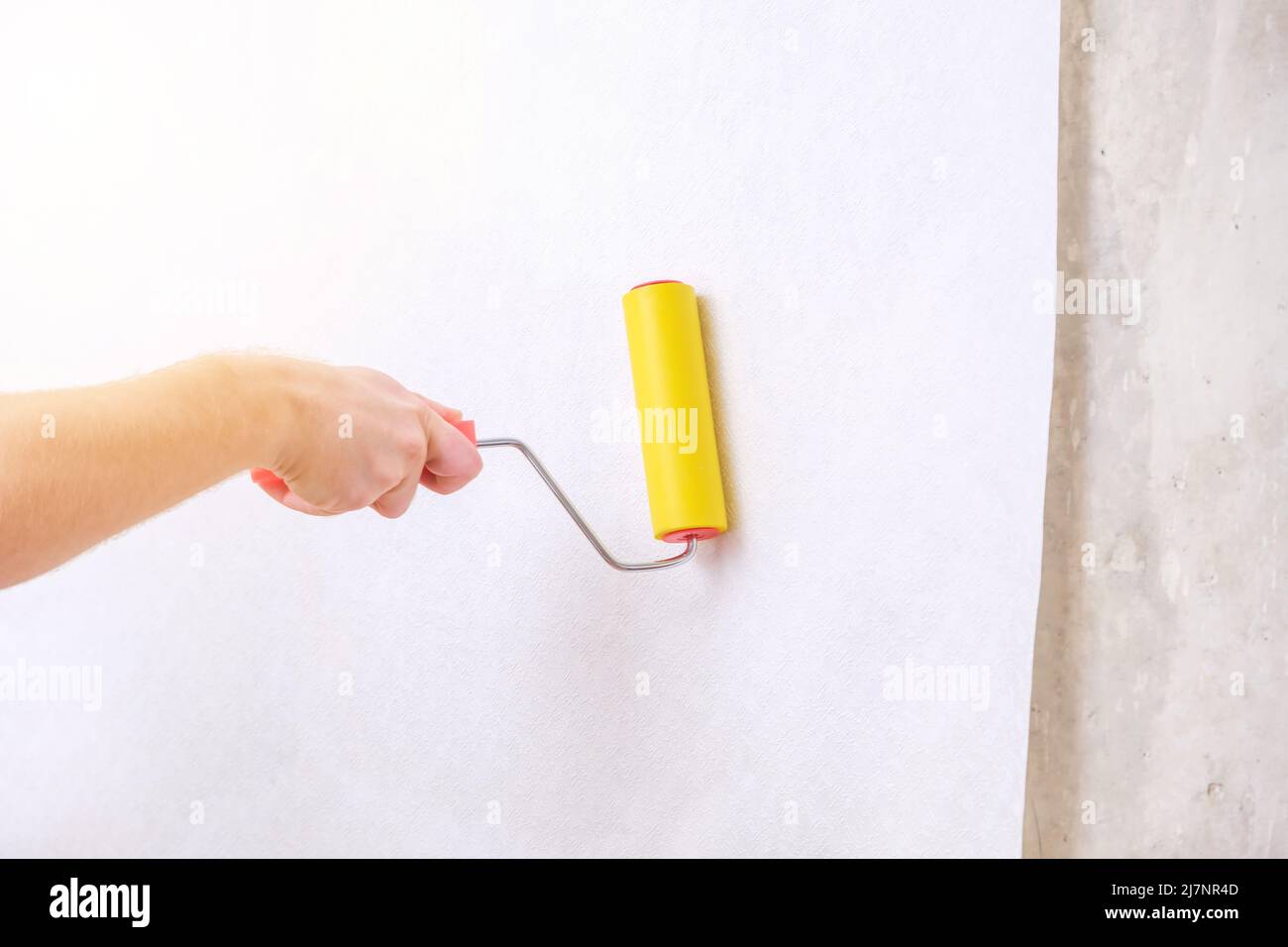 A man rolls out a canvas of white wallpaper with a suture yellow roller