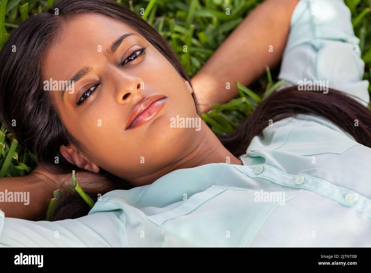 Outdoor portrait of a beautiful Indian Asian young woman or girl outside in summer sunshine laying down on grass Stock Photo