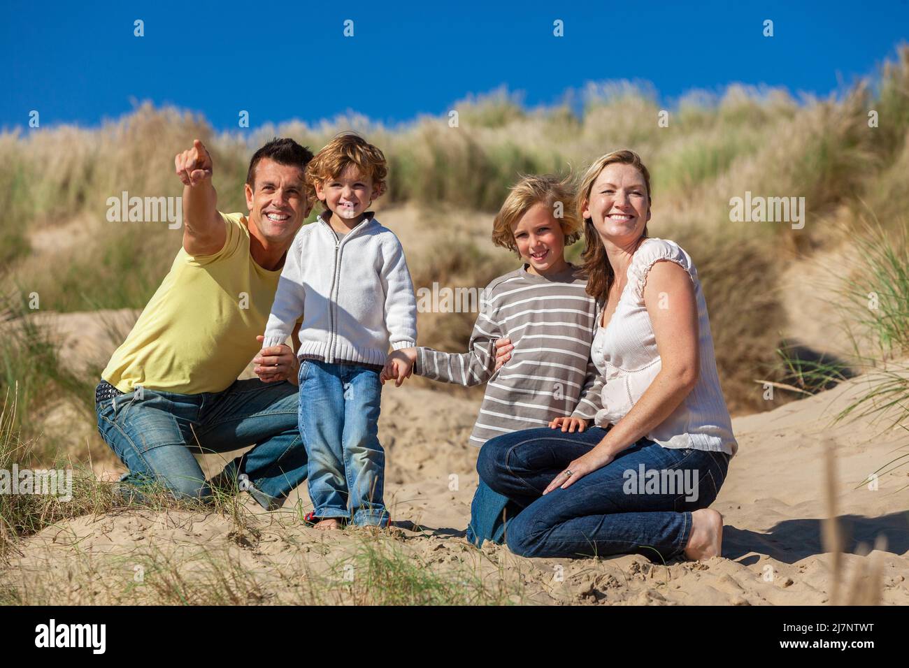 Happy family of mother, father and two sons, man woman children on vacation, having fun in the sand dunes of a sunny beach Stock Photo