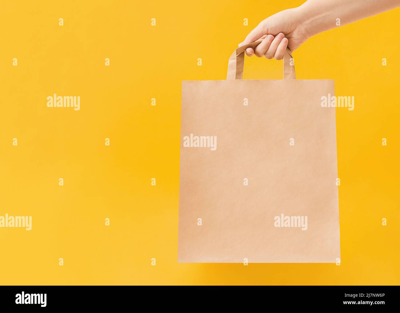 Woman is holding paper bag with handles on yellow backdrop Stock Photo