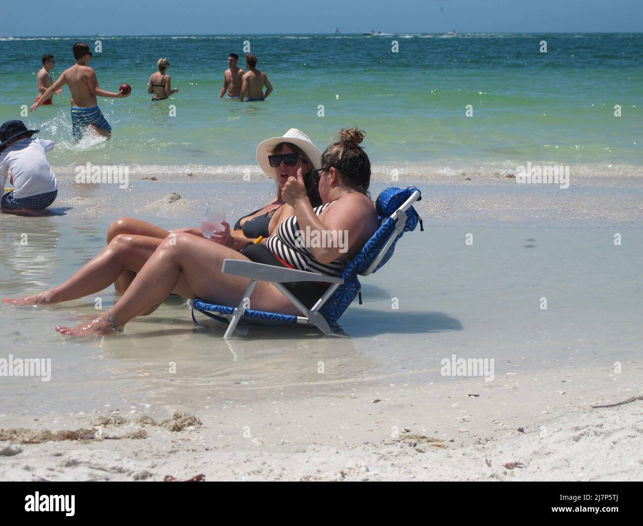 Young women enjoying the waves of the ocean waters on sun chairs Stock Photo