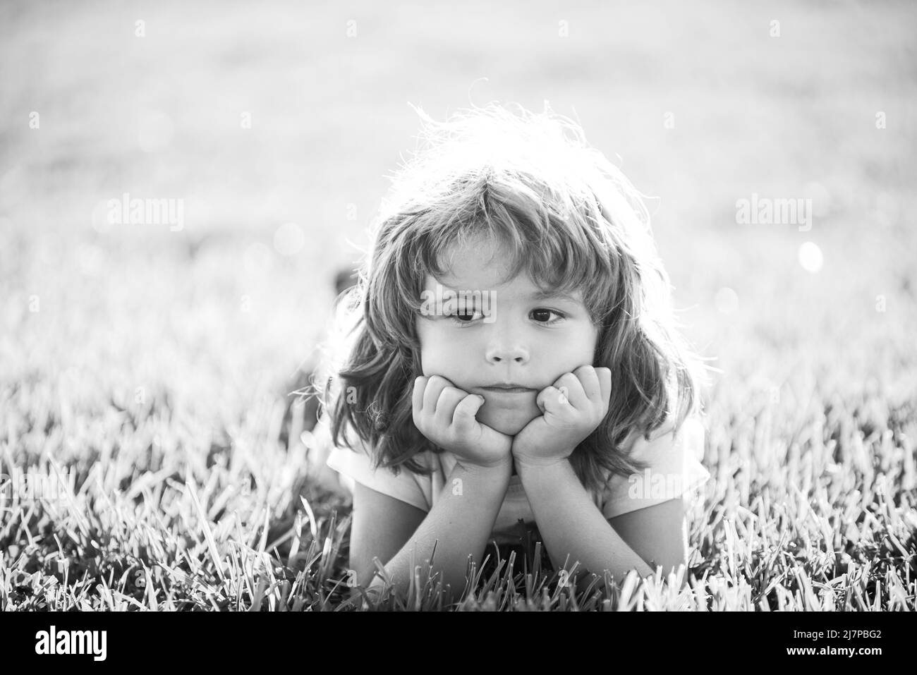 Kid in park. Child outdoor. Spring Boy lying on grass. Summer walk. Children adaptation. Stock Photo