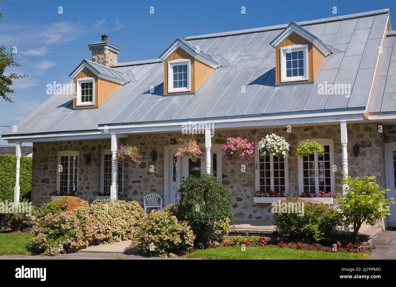 Replica of old 1800s Canadiana cottage style fieldstone home with white trim and silver sheet