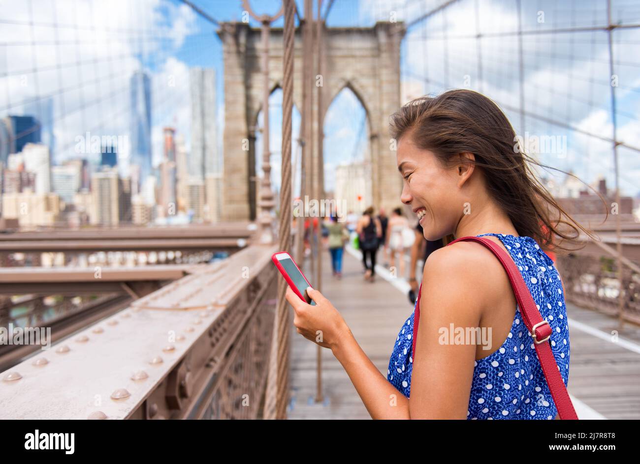 New York tourist woman using phone app walking on Brooklyn Bridge towards Manhattan city skyline. Young female professional multicultural lady, New Stock Photo