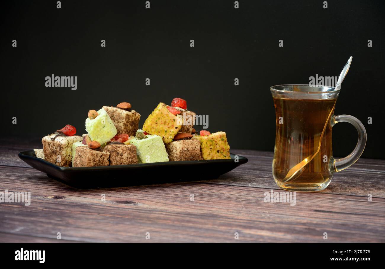 An assortment of Turkish sweets on a plate and a cup of hot black tea on a wooden table. Close-up. Stock Photo