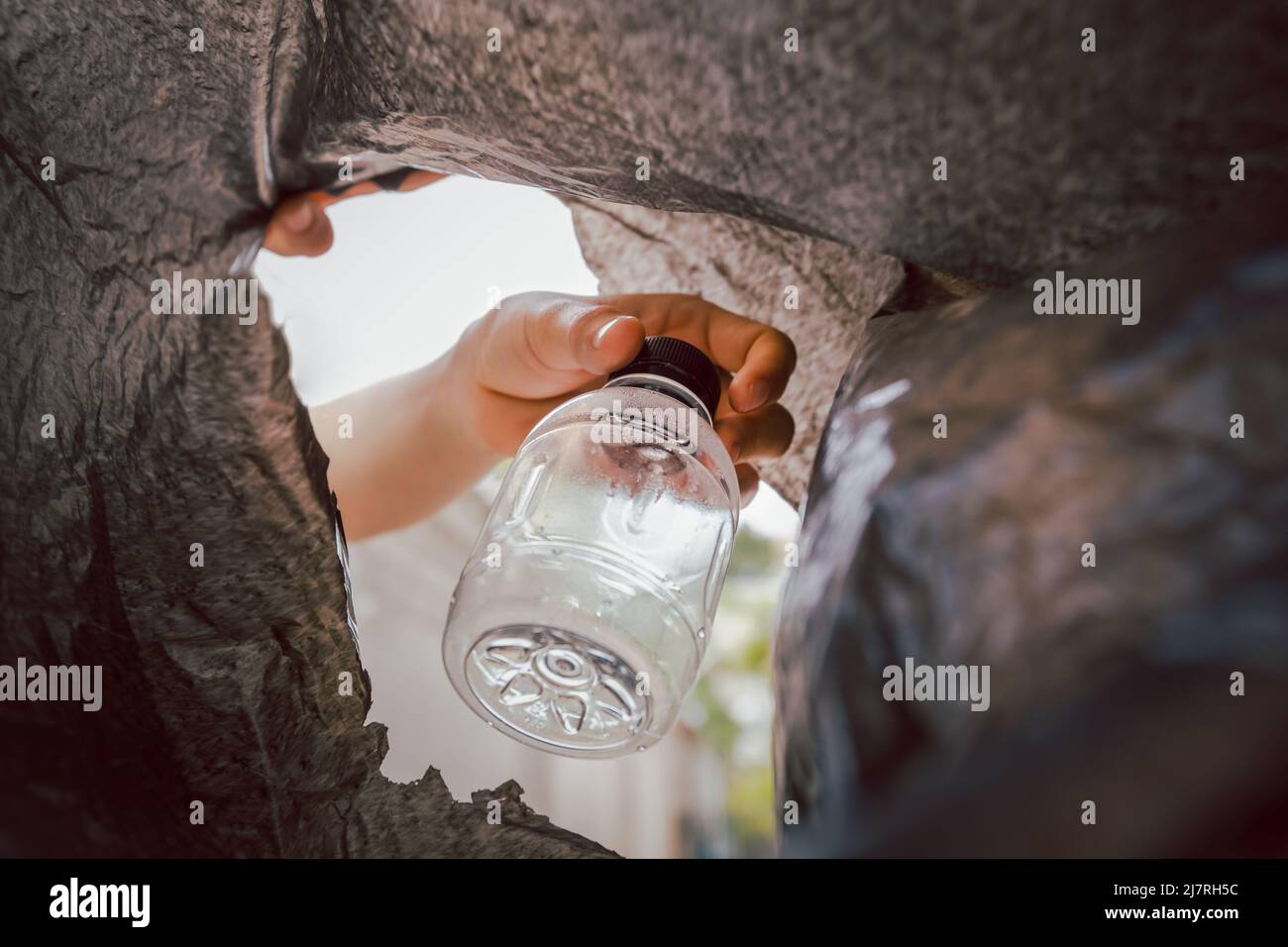 Hand putting plastic bottle in a black bag for recycling Stock Photo