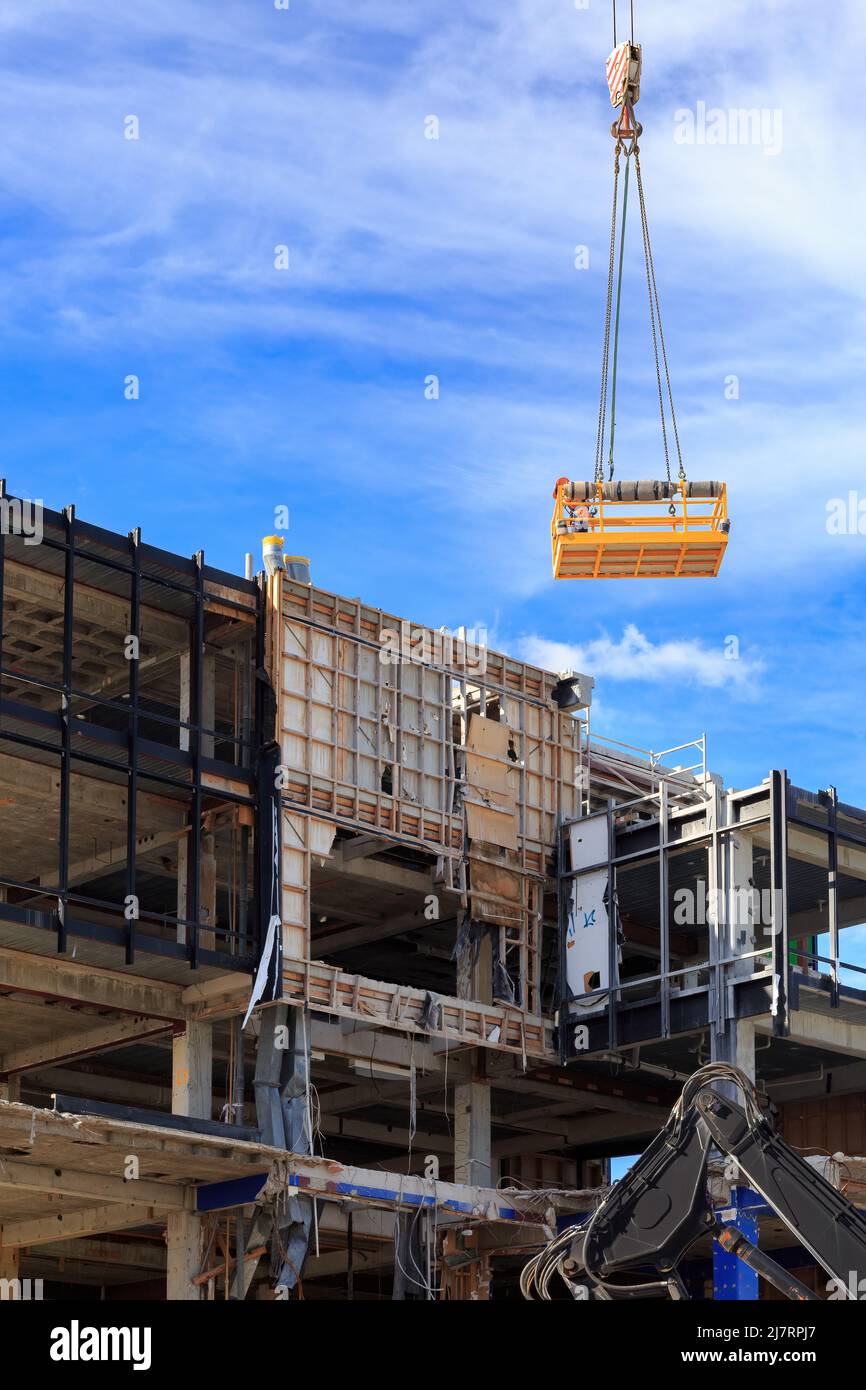 A demolition worker on a work platform, being lowered by crane to the remains of a partially dismantled office building Stock Photo