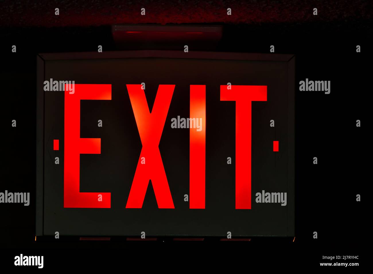 An exit sign over a doorway to the outside in a dark hallway. Stock Photo