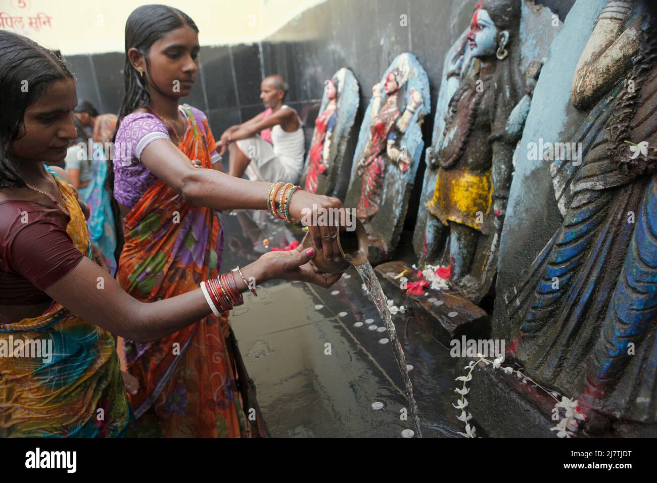 Women pilgrims pouring water in front of Indian deities after taking a