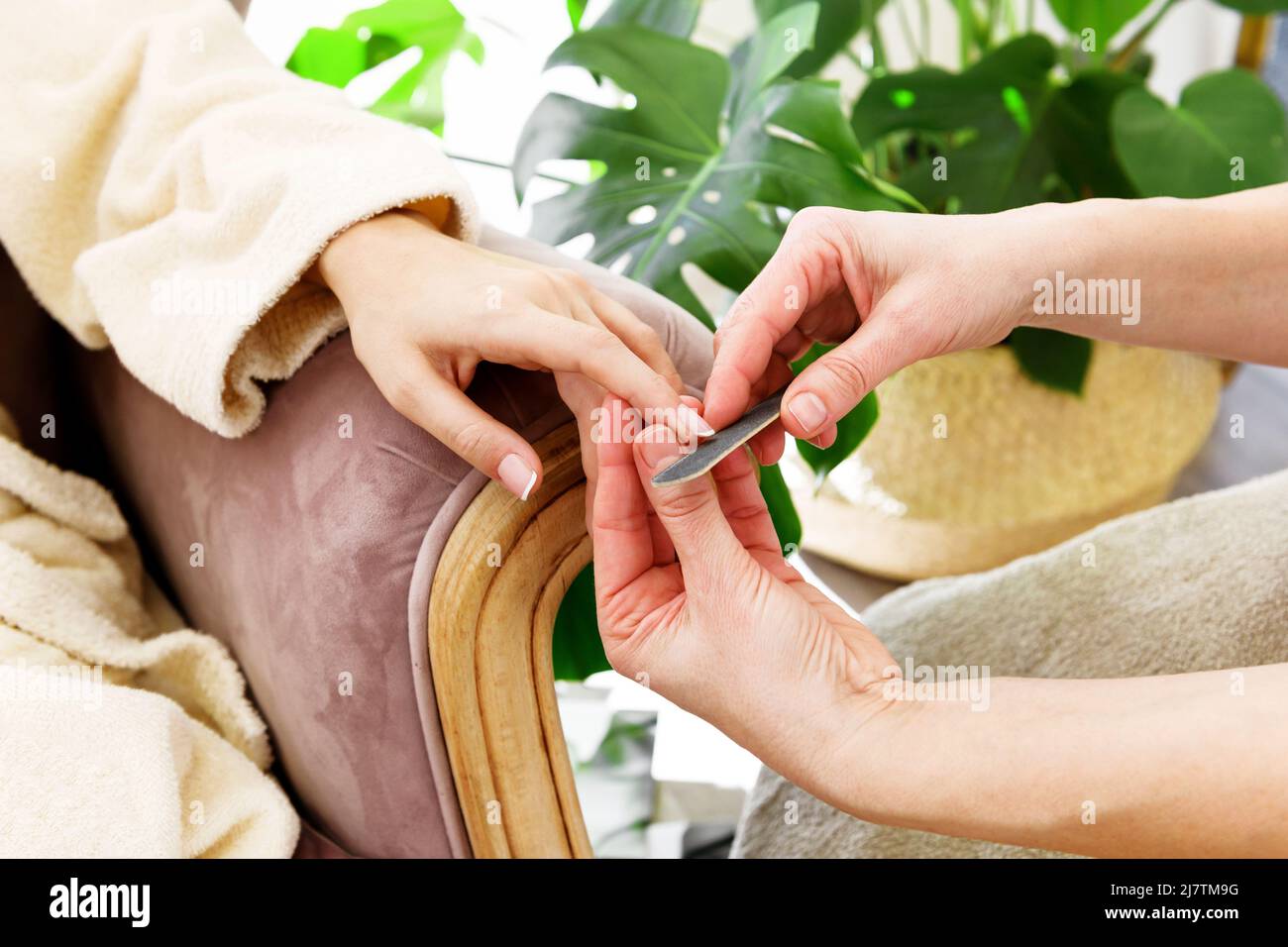 Crop anonymous master with nail file sawing nails of unrecognizable female client sitting in armchair during appointment in beauty salon Stock Photo