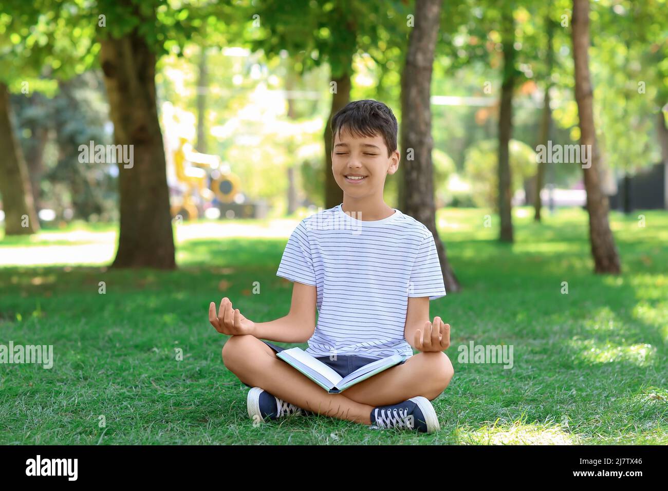 Little boy with book meditating in park Stock Photo