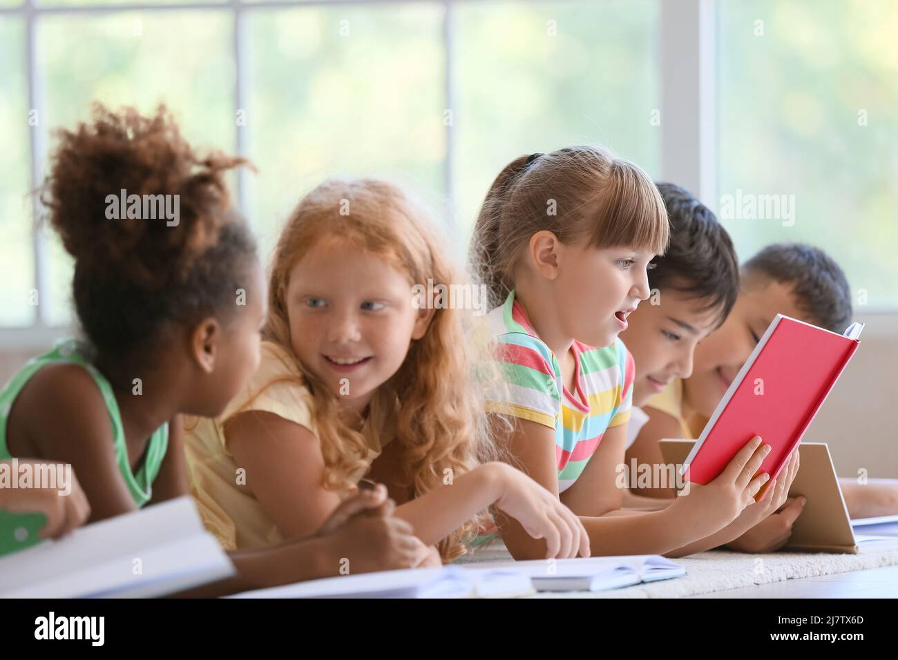 Cute little children reading books on floor in classroom Stock Photo