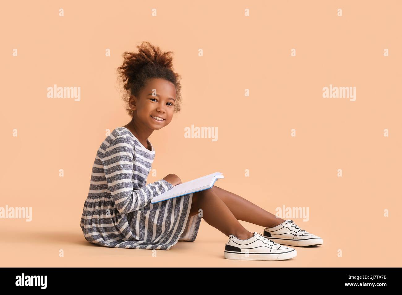 Little African-American girl reading book on beige background Stock ...