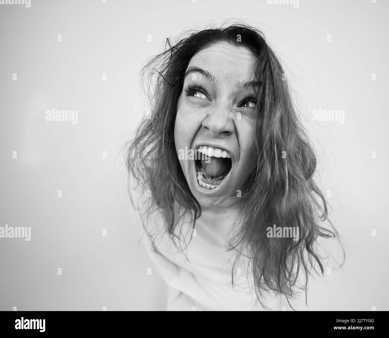 Close-up portrait of insane woman in straitjacket on white background. Monochrome. Stock Photo