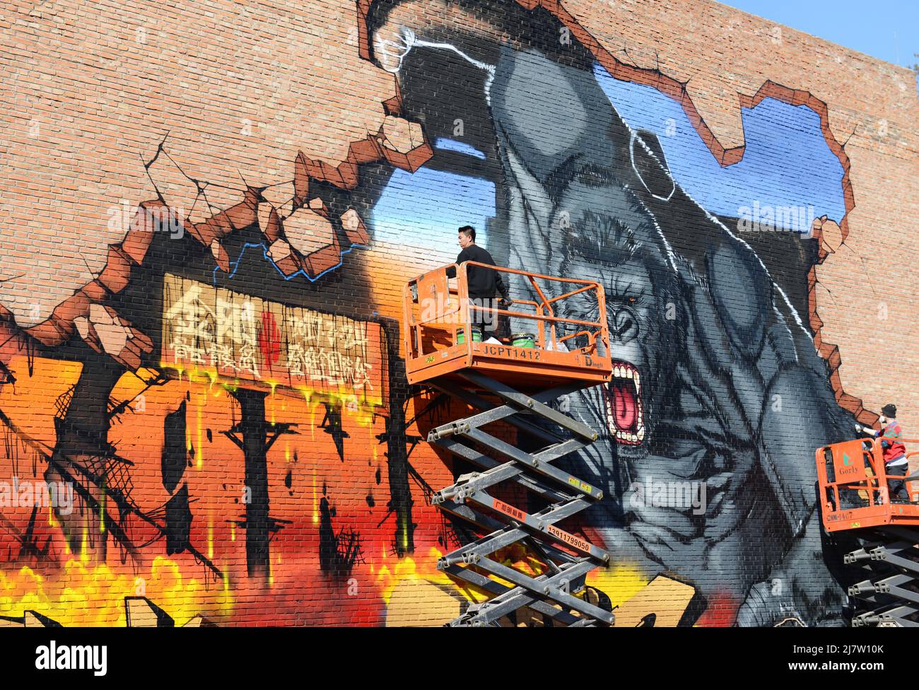 An artist painting a King Kong graffiti on on old brick factory building ( Joy Art building ) in the 798 Art Zone in Beijing, China. Stock Photo