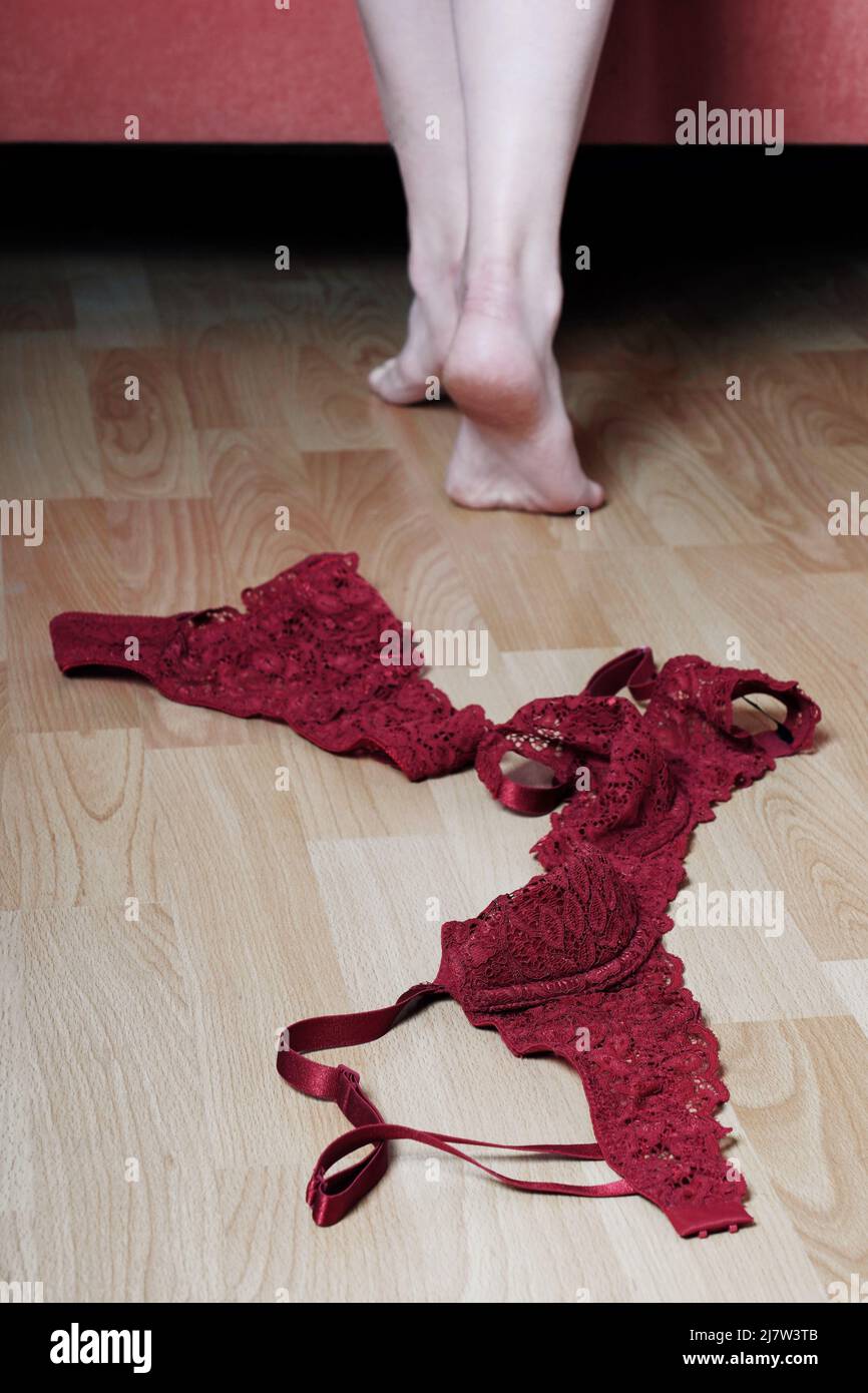 bra and panties lying on bedroom floor while female feet walking towards bed Stock Photo