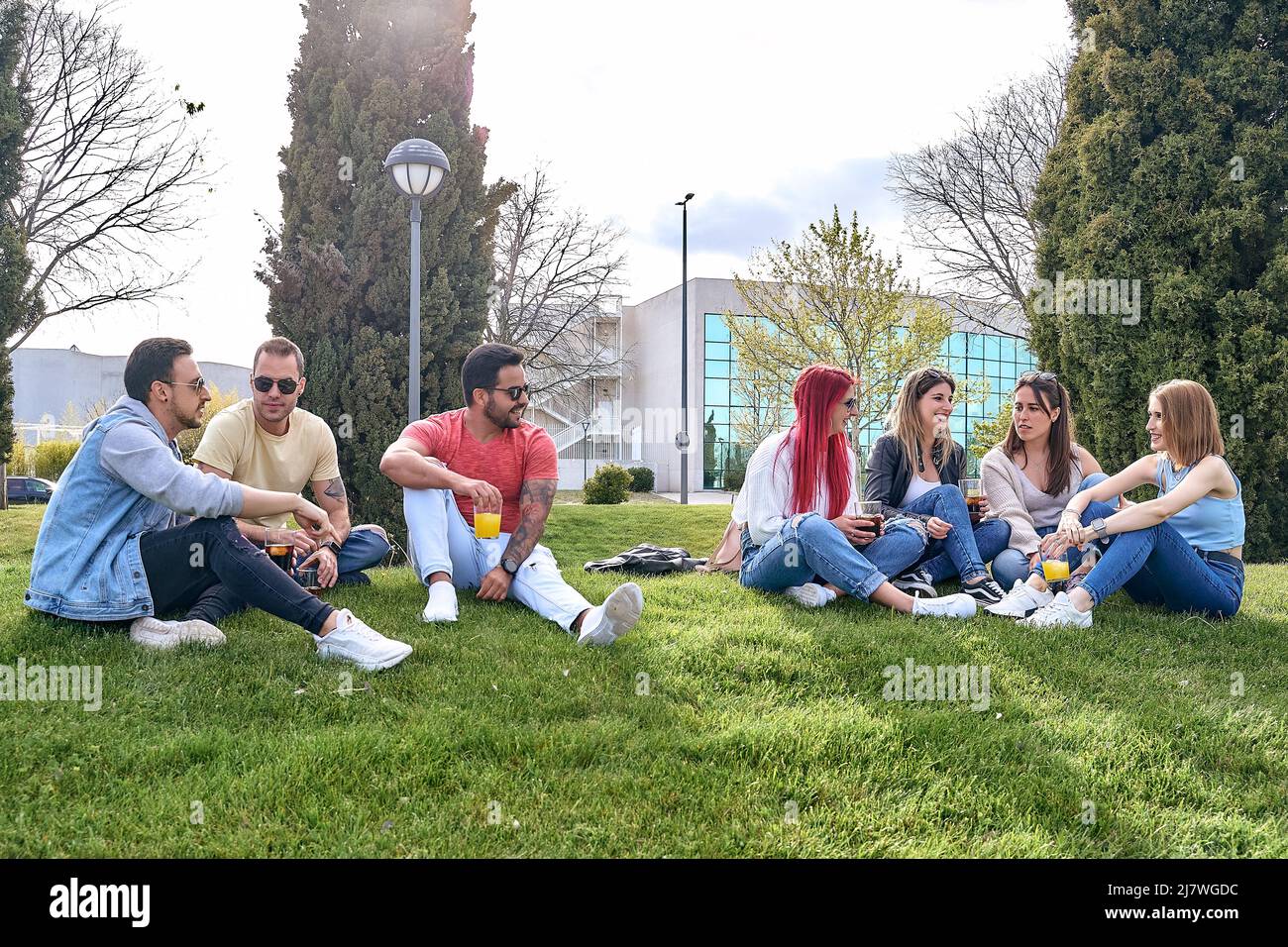 Group of guys sitting in a park next to a group of girls, drinking and hanging out on a sunny day. High quality photo Stock Photo