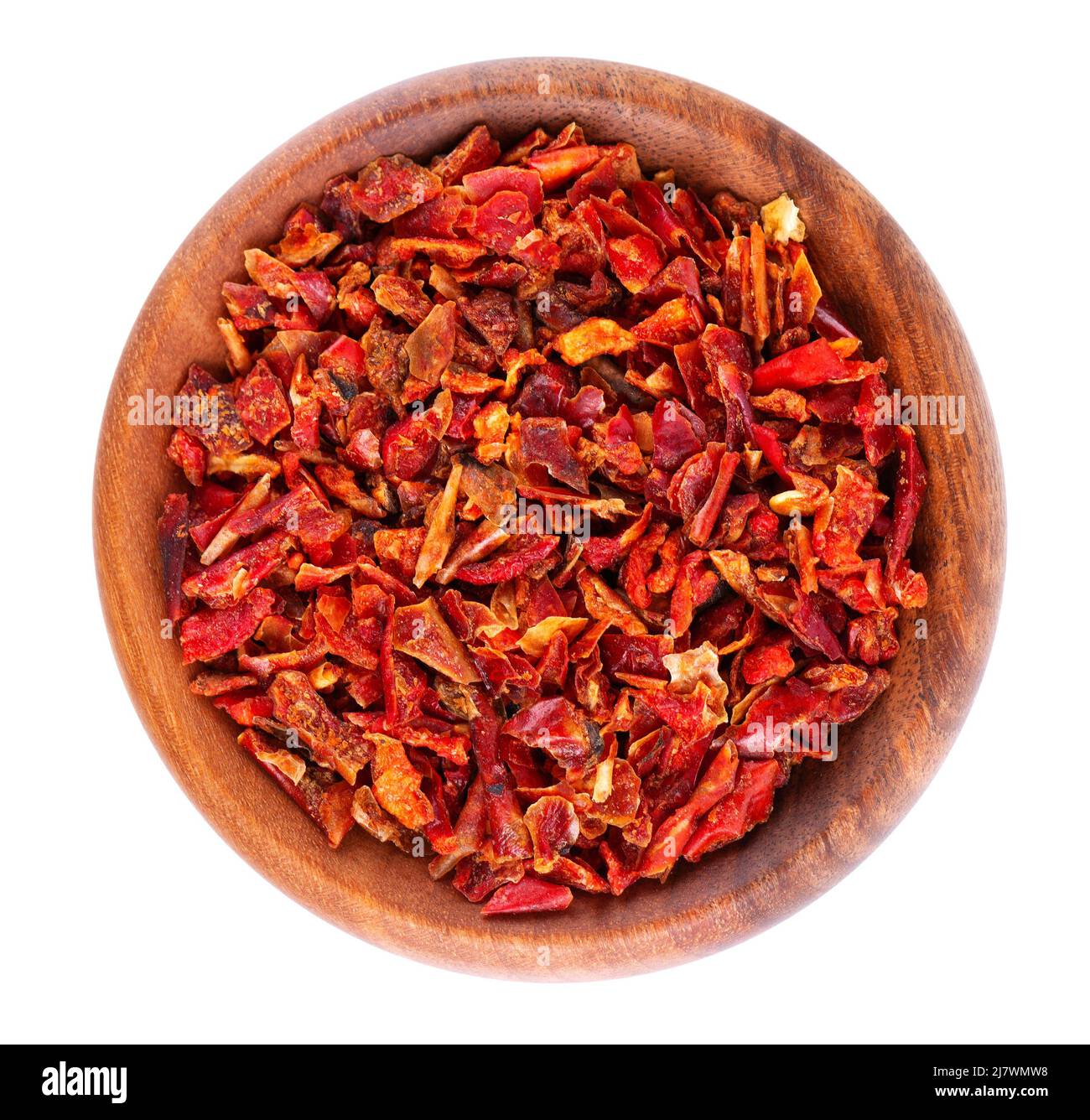 Dried red paprika flakes in wooden bowl, isolated on white background